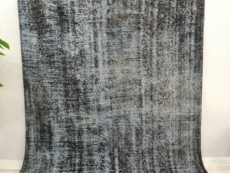 May include: A vintage rug with a distressed, faded look. The rug has a black and white color scheme with a subtle blue undertone. The rug has a textured, woven appearance.