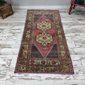 May include: A vintage runner rug with a pink, cream, and brown geometric pattern. The rug has a distressed look and is perfect for adding a touch of bohemian style to your home.
