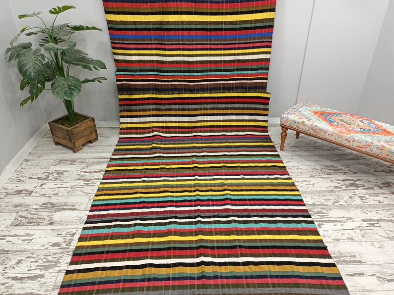 May include: A long, rectangular striped rug with a variety of colors, including red, yellow, blue, green, and brown. The rug is made of a woven fabric and has a fringed edge.