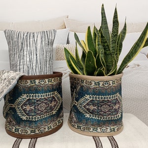 May include: Two teal blue and brown patterned fabric storage baskets with a beige trim. One basket holds a potted snake plant with green and yellow leaves. The other basket holds a gray and white throw blanket.