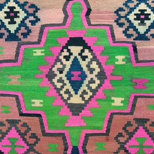 Puede incluir: Una alfombra colorida con un patr&oacute;n geom&eacute;trico en tonos de rosa, verde, negro y blanco. La alfombra tiene una forma de diamante central con un diamante m&aacute;s peque&ntilde;o en su interior.