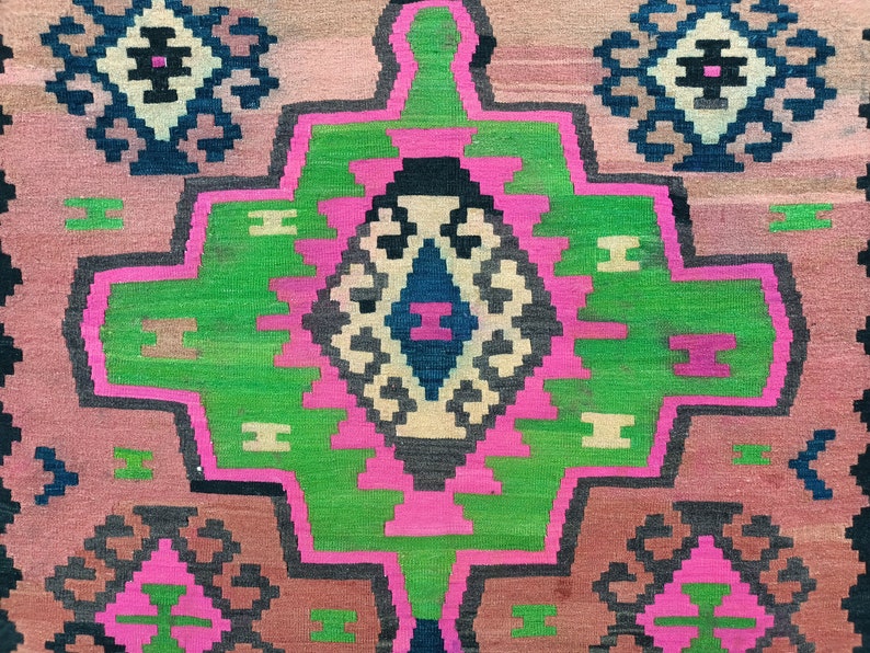 Puede incluir: Una alfombra colorida con un patr&oacute;n geom&eacute;trico en tonos de rosa, verde, negro y blanco. La alfombra tiene una forma de diamante central con un diamante m&aacute;s peque&ntilde;o en su interior.