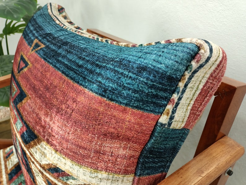 K&ouml;nnte beinhalten: Nahaufnahme eines gemusterten Kissens auf einem Holzstuhl. Das Kissen hat ein geometrisches Design mit t&uuml;rkisfarbenen, roten und beigen Streifen und Dreiecken. Der Stuhl hat eine dunkle Holzoberfl&auml;che.