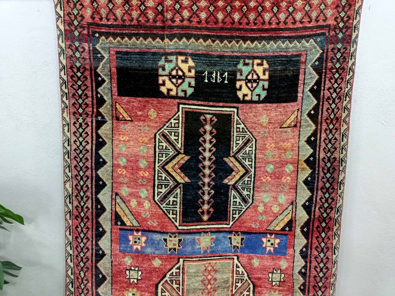 May include: A red, blue, and black patterned rug with a geometric design. The rug has a border with a repeating pattern of diamonds and squares. The rug has the number "1381" written in the center.