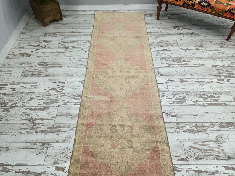 May include: A vintage runner rug with a faded pink and cream colour scheme. The rug has a traditional floral pattern with a diamond shape in the centre.