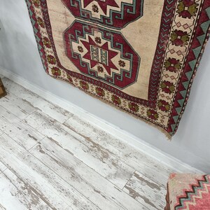 May include: A vintage rug with a beige background and intricate red, green, and blue geometric patterns. The rug is hanging on a light gray wall.