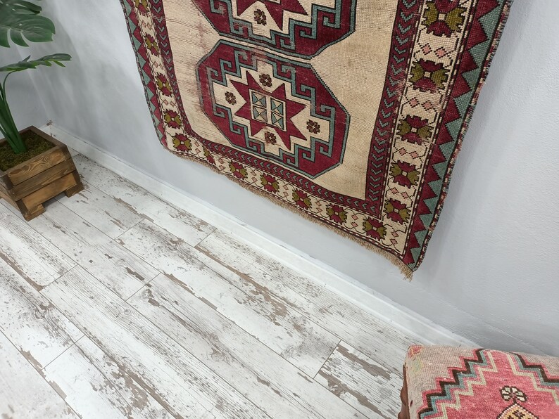 May include: A vintage rug with a beige background and intricate red, green, and blue geometric patterns. The rug is hanging on a light gray wall.
