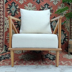 May include: A white upholstered armchair with a wooden frame and legs. The chair has a white cushion and is set against a red and black patterned rug.