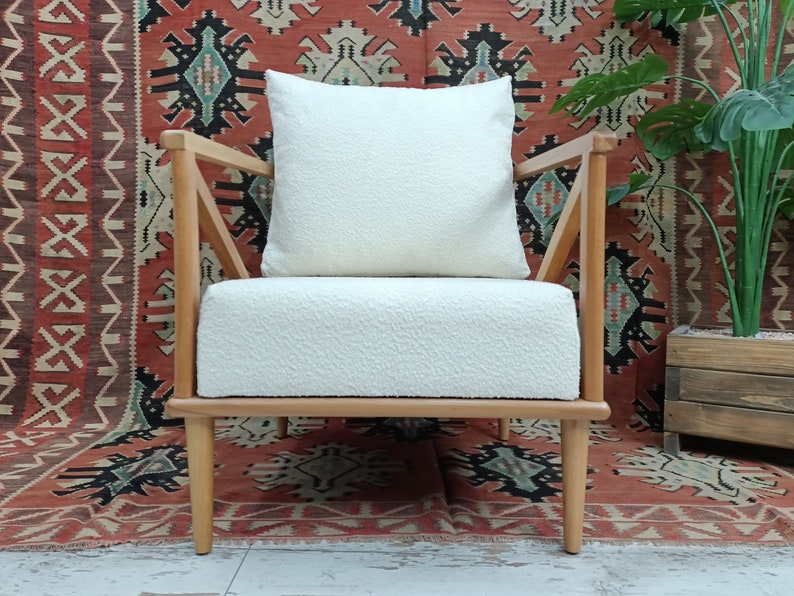 May include: A white upholstered armchair with a wooden frame and legs. The chair has a white cushion and is set against a red and black patterned rug.