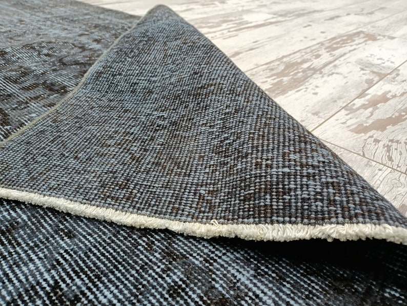 May include: Close-up of a blue and brown woven rug with a white fringe. The rug is folded in half, showing the back side of the rug.