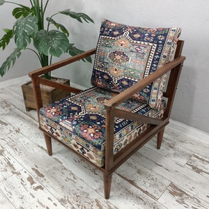 Puede incluir: Un sill&oacute;n de madera con un marco marr&oacute;n oscuro y un coj&iacute;n estampado. El coj&iacute;n presenta un dise&ntilde;o colorido con acentos azules, rojos y blancos. El sill&oacute;n est&aacute; sentado en un suelo de madera blanqueada.