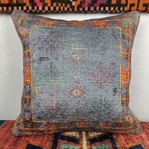Op de afbeelding: Een decoratief kussen met een blauwe achtergrond en een kleurrijk geometrisch patroon. Het kussen heeft een rode, oranje en gele rand.