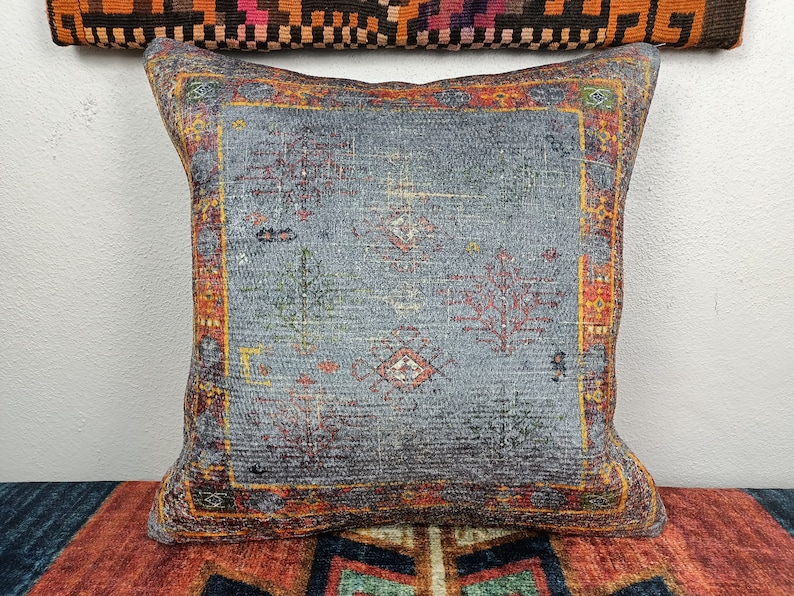 Op de afbeelding: Een decoratief kussen met een blauwe achtergrond en een kleurrijk geometrisch patroon. Het kussen heeft een rode, oranje en gele rand.