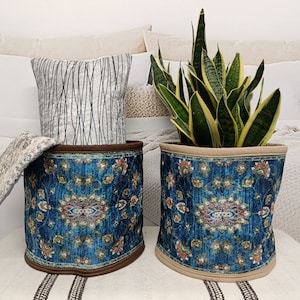 May include: Two blue and brown patterned fabric storage baskets with a beige top rim. One basket holds a potted snake plant with green leaves and yellow edges. The baskets are sitting on a white surface.