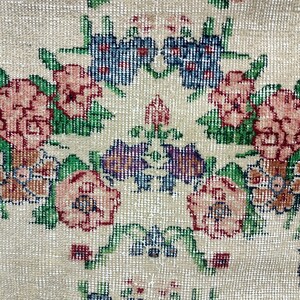 May include: A vintage rug with a floral pattern in shades of pink, green, blue, and brown. The rug has a cream background and a woven texture.