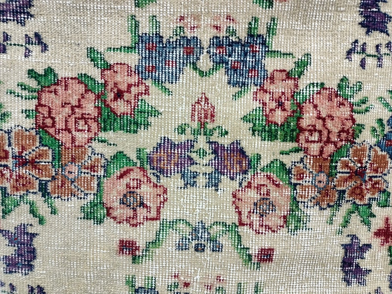 May include: A vintage rug with a floral pattern in shades of pink, green, blue, and brown. The rug has a cream background and a woven texture.