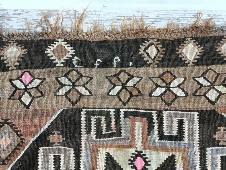 May include: Close-up of a brown and black rug with a geometric pattern. The rug has a fringe border and the letters "E F P" are woven into the rug.
