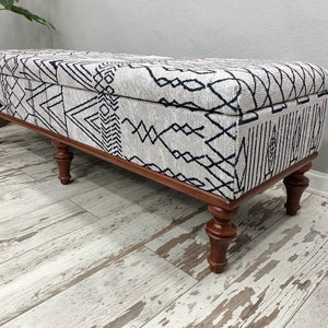 May include: A long, rectangular storage bench with a white and black geometric patterned fabric top and four wooden legs.