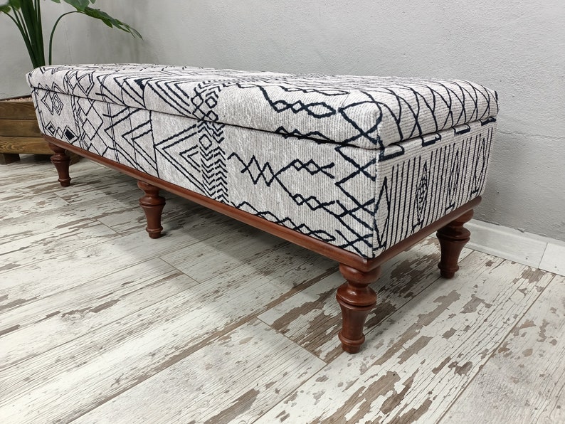 May include: A long, rectangular storage bench with a white and black geometric patterned fabric top and four wooden legs.