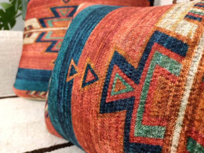 K&ouml;nnte beinhalten: Zwei Dekokissen mit einem s&uuml;dwestlichen Muster mit geometrischen Formen in Orange-, Rot-, Blau-, Gr&uuml;n- und Wei&szlig;t&ouml;nen.