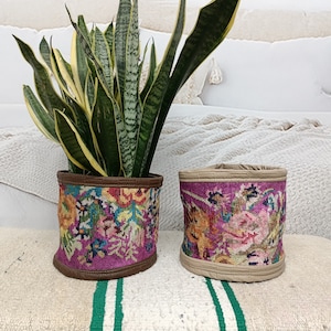 May include: Two colorful floral patterned fabric plant pots with a brown leather trim. The pot on the left is holding a green snake plant.