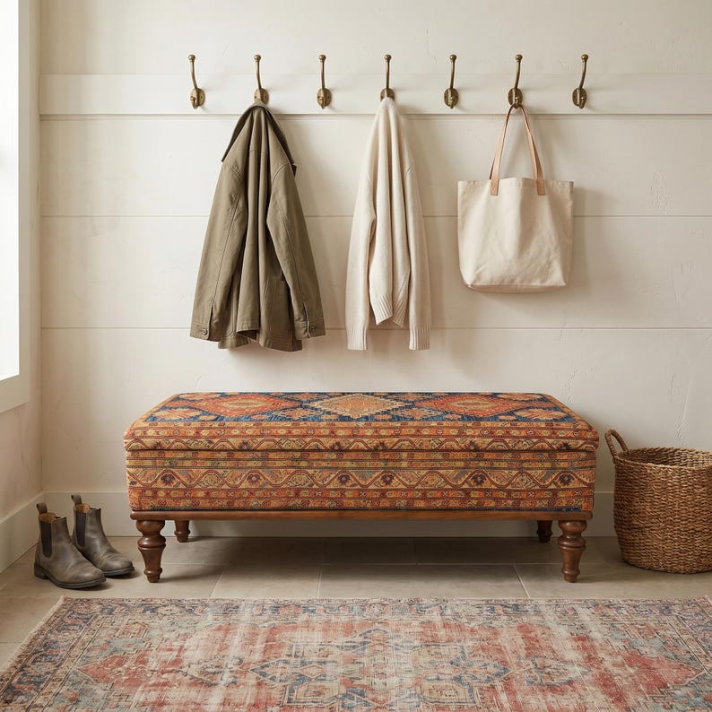 a cozy entryway with a wooden bench, a woven basket, and a pair of boots. The bench has a colorful, patterned seat and is positioned in front of a wall with six hooks for hanging coats and bags.