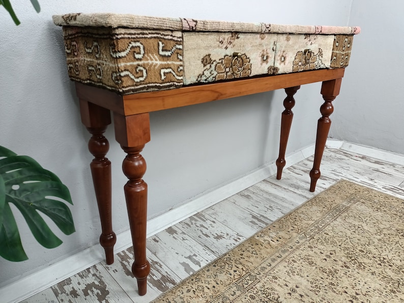 Op de afbeelding: Een houten consoletafel met een blad van patchwork stof. De tafel heeft gedraaide poten met een balvormige knop.