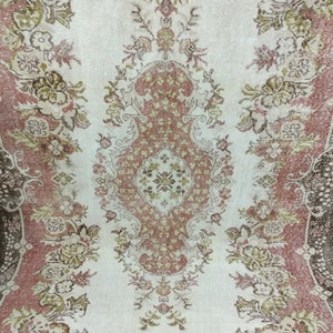 Op de afbeelding: Een vintage tapijt met een bloemenpatroon in tinten roze, bruin en cr&egrave;me. Het tapijt heeft een verweerde uitstraling en een verbleekte uitstraling.