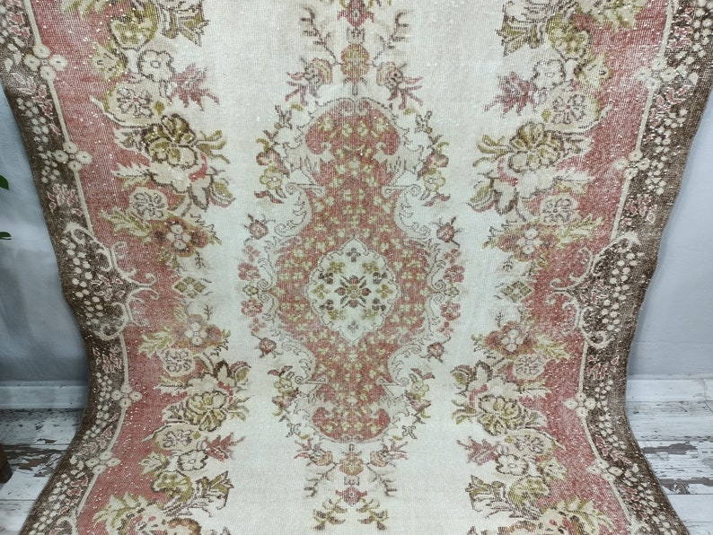 Op de afbeelding: Een vintage tapijt met een bloemenpatroon in tinten roze, bruin en cr&egrave;me. Het tapijt heeft een verweerde uitstraling en een verbleekte uitstraling.