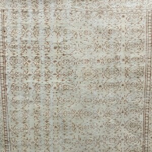 Puede incluir: Una alfombra blanca con un patr&oacute;n floral marr&oacute;n. La alfombra tiene un borde marr&oacute;n y blanco.