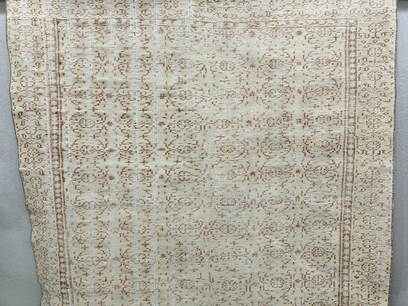 Puede incluir: Una alfombra blanca con un patr&oacute;n floral marr&oacute;n. La alfombra tiene un borde marr&oacute;n y blanco.