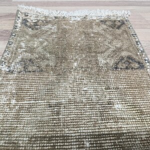 May include: A beige and brown woven rug with a fringed edge. The rug has a faded pattern with a geometric design.