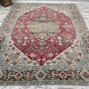May include: A vintage rug with a red, cream, and brown geometric pattern. The rug has a detailed floral design and a border with a blue and cream pattern.