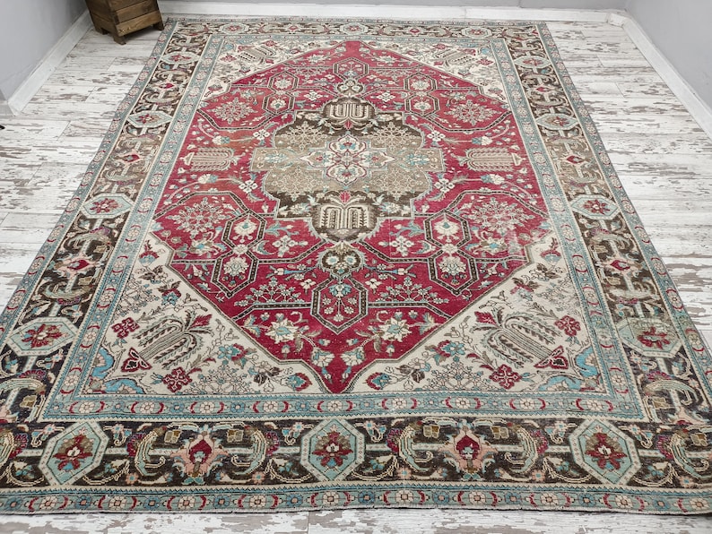 May include: A vintage rug with a red, cream, and brown geometric pattern. The rug has a detailed floral design and a border with a blue and cream pattern.