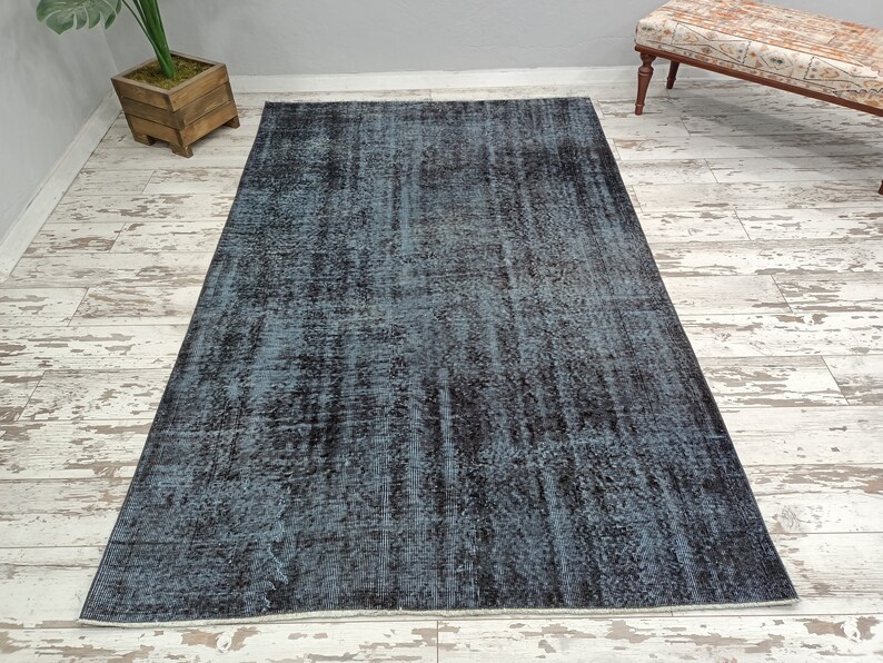 May include: A distressed vintage rug with a blue and black color scheme. The rug has a faded, worn look and a subtle pattern.