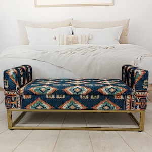 May include: A blue upholstered bench with a geometric pattern in orange, green, and white. The bench has a gold metal frame and is placed at the foot of a bed. The bench measures approximately 48 inches long.