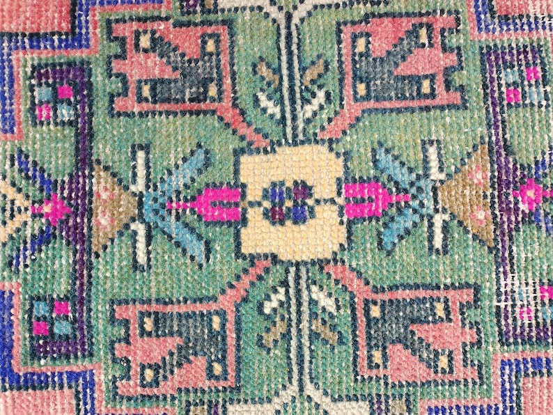Peut inclure: Gros plan sur un tapis color&eacute; avec un motif g&eacute;om&eacute;trique. Le tapis est fait de tissu tiss&eacute; et pr&eacute;sente des nuances de rose, bleu, vert et jaune.