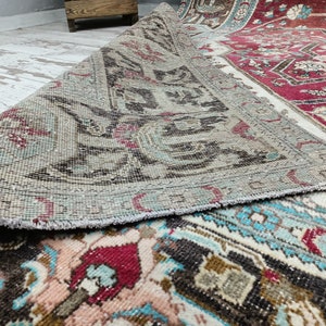 May include: A vintage rug with a faded, light blue and brown pattern. The rug has a fringed edge and is rolled up, revealing a red and white patterned underside.