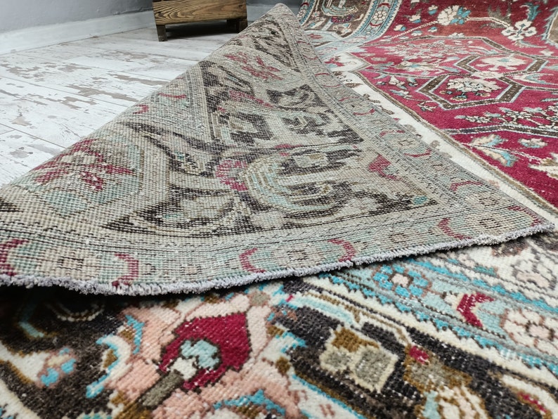 May include: A vintage rug with a faded, light blue and brown pattern. The rug has a fringed edge and is rolled up, revealing a red and white patterned underside.