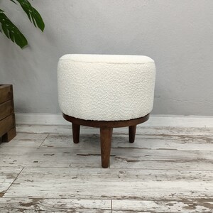 Puede incluir: Otomana redonda blanca con textura esponjosa y cuatro patas de madera.