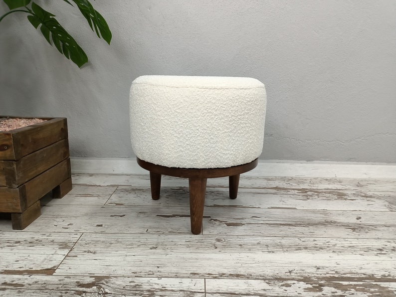 Puede incluir: Otomana redonda blanca con textura esponjosa y cuatro patas de madera.
