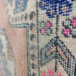 Pode incluir: Close-up de um tapete rosa e branco com um padr&atilde;o floral azul e verde. O tapete tem uma borda de franjas.