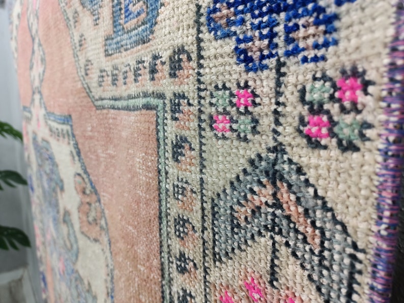 Pode incluir: Close-up de um tapete rosa e branco com um padr&atilde;o floral azul e verde. O tapete tem uma borda de franjas.