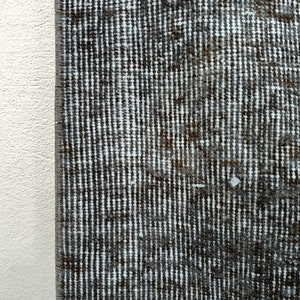 May include: Close-up of a dark gray rug with a white and gray striped pattern. The rug has a textured surface and is made of woven fibers.