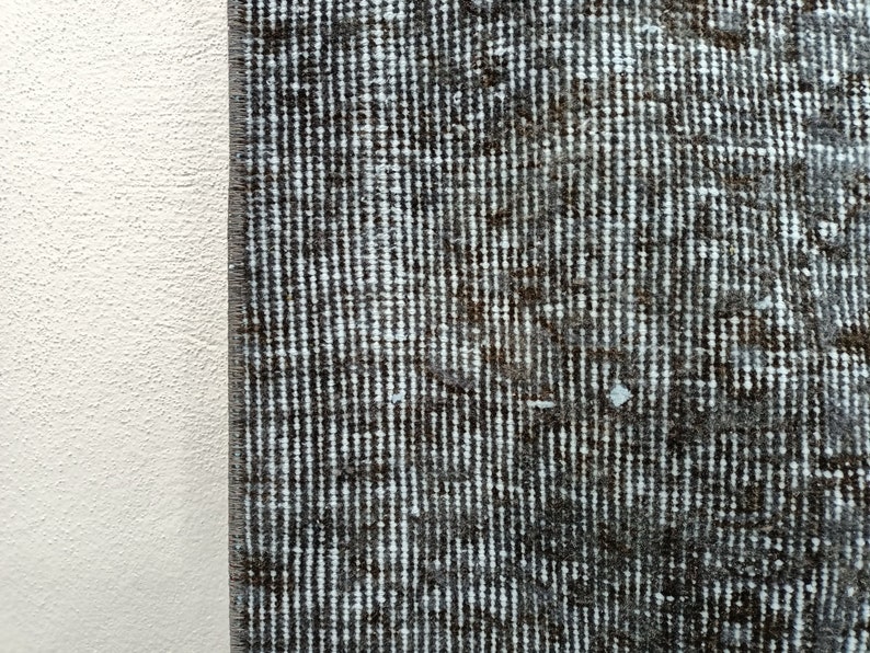 May include: Close-up of a dark gray rug with a white and gray striped pattern. The rug has a textured surface and is made of woven fibers.