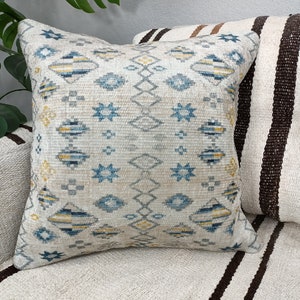 May include: A white throw pillow with a blue and yellow geometric pattern. The pillow is sitting on a striped couch.