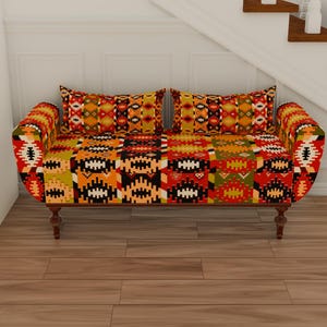 May include: A two-seater sofa with a vibrant, patterned fabric in shades of red, orange, yellow, and black. The sofa has a curved back and armrests, with two matching throw pillows. The wooden legs add a touch of elegance to the overall design.