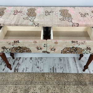 Op de afbeelding: Een houten consoletafel met twee laden. De bovenkant en de laden zijn bedekt met een gepatenteerde stof in roze, bruin en witte kleuren. De tafel heeft vier houten poten.