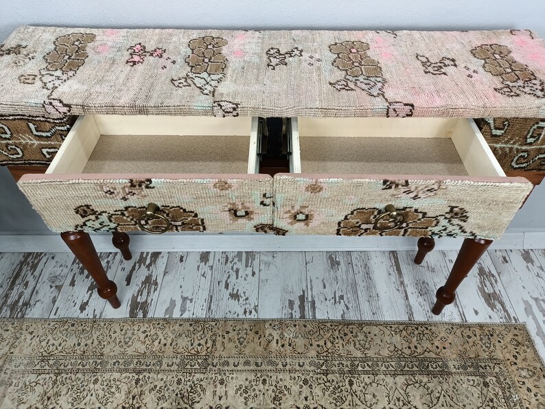 Op de afbeelding: Een houten consoletafel met twee laden. De bovenkant en de laden zijn bedekt met een gepatenteerde stof in roze, bruin en witte kleuren. De tafel heeft vier houten poten.