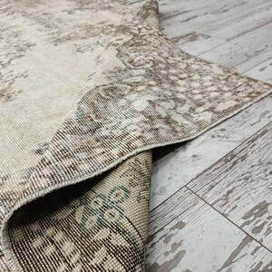 May include: A close-up of a beige and brown patterned rug with a frayed edge. The rug is folded over and the underside is visible.